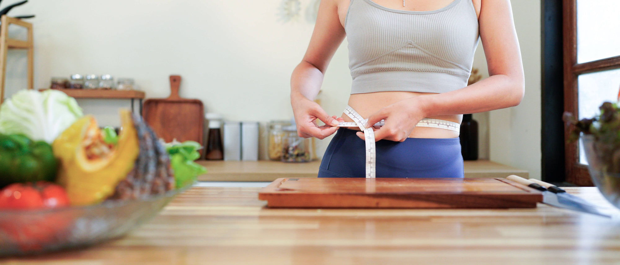 Person measuring waist in a kitchen with high fiber food on the counter